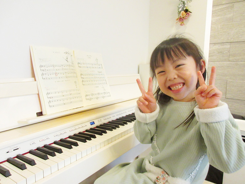 ピアノの前で笑顔でピースする女の子の生徒さんの写真